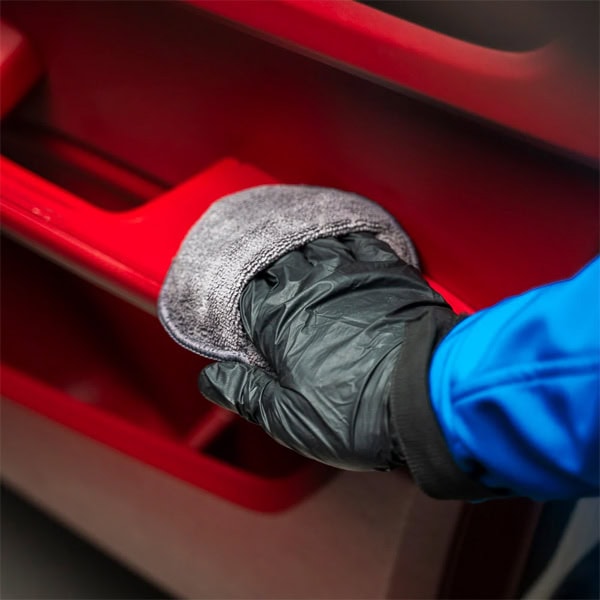 Worker cleaning red plastic storage bin with cloth, focusing on building materials.