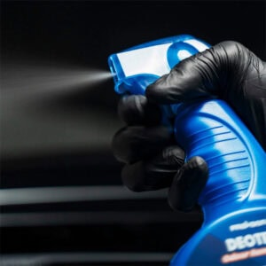 Hand holding a blue spray bottle for cleaning building surfaces, close-up shot.