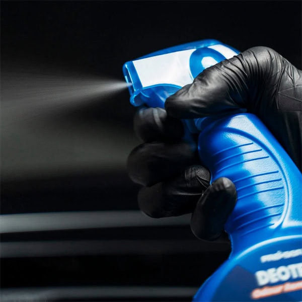 Hand holding a blue spray bottle for cleaning building surfaces, close-up shot.