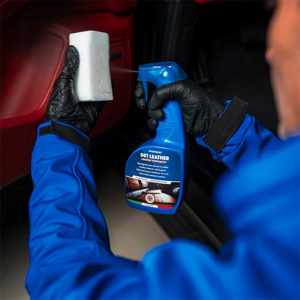 Person cleaning car interior leather with spray and cloth.