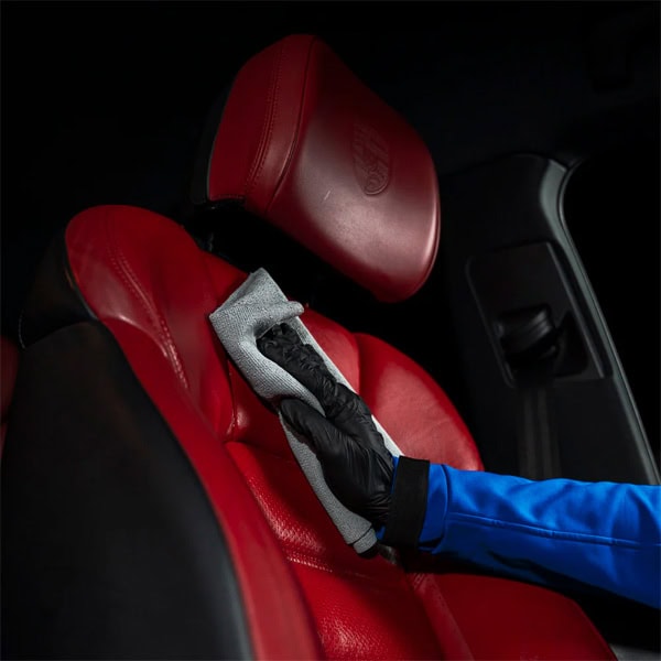 Person cleaning red car seat with microfiber cloth for interior maintenance.