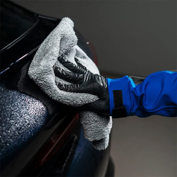 Hand polishing a car with microfiber cloth, close-up of car detailing process.