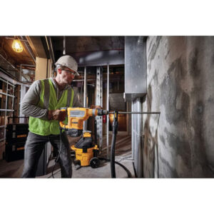 Construction worker operating a power drill on a building site with concrete walls.