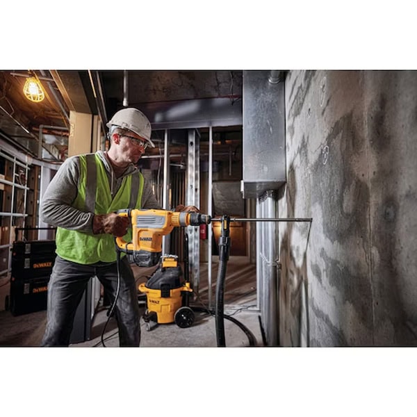 Construction worker operating a power drill on a building site with concrete walls.