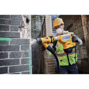 Construction worker drilling into brick wall with safety gear.