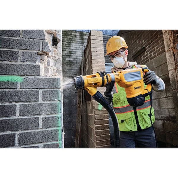 Construction worker drilling into brick wall with safety gear.