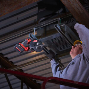 Worker installing metal roofing sheet with power saw at construction site.